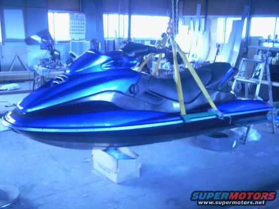 Blue jet ski suspended by yellow straps in a workshop